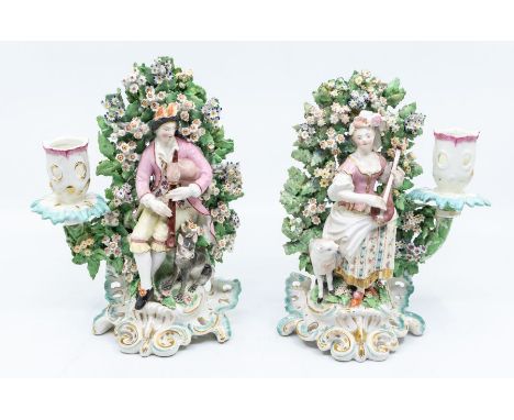 A pair of Derby porcelain figural candlesticks modelled as a seated Gentleman playing the bag pipes with dog by his side and 