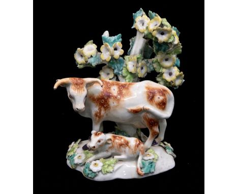 An 18th Century Chelsea Derby porcelain model of a Cow with recumbent calf, the bodies with brown patches, bocage behind with