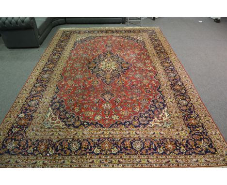 Kashan carpet, central medallion on a flower field red ground, border within guards, 413cm x 283cm.