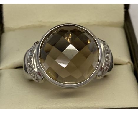 A silver cocktail ring set with checkerboard cut smoked quartz and diamonds. Central round bezel set smoked quartz with 3 sma