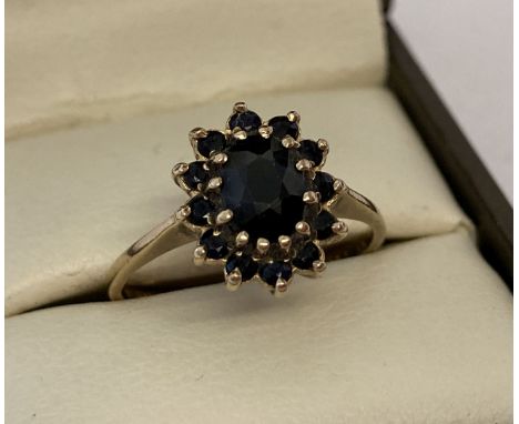 A 9ct gold and sapphire dress ring. Central oval cut sapphire surrounded by 12 small round cut sapphires. Hallmarks to inside