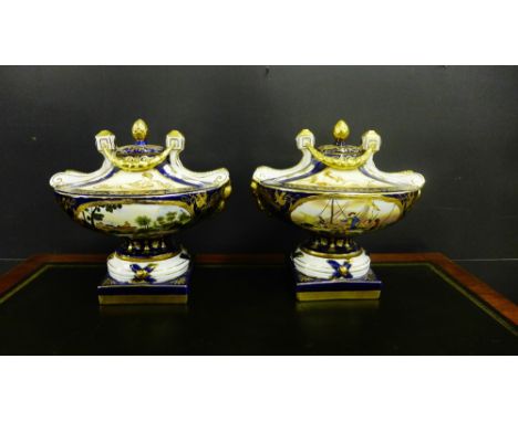 A pair of porcelain urns with figures to the front against a blue and gilded ground, the lid with acorn finial complete with 