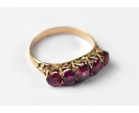 A yellow metal five-stone ruby ring, with a row of five graduated facet cut rubies within scroll mounts, on an unmarked yello