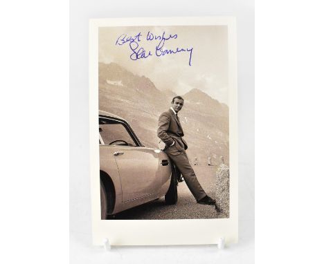 SEAN CONNERY; a black and white photographic postcard bearing the star's signature, leaning on an Aston Martin whilst playing