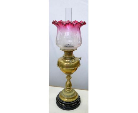 A VICTORIAN BRASS OIL LAMP WITH BALUSTER PILLAR ON BLACK GLAZED EARTHENWARE FOOT, BRASS BURNER, CONTEMPORARY ETCHED CRANBERRY