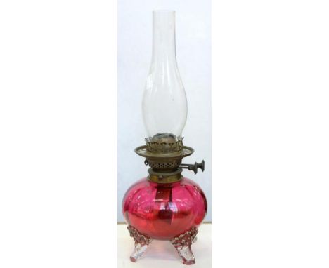 A VICTORIAN GLOBULAR CRANBERRY GLASS OIL LAMP ON THREE CLEAR FEET, WITH BRASS BURNER, 22CM H EXCLUDING CHIMNEY, C1880
