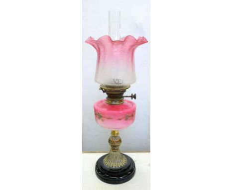 A VICTORIAN ENAMELLED SHADED PINK CASED GLASS AND BRASS MOUNTED OIL LAMP ON BLACK GLAZED EARTHENWARE FOOT WITH BRASS BURNER A