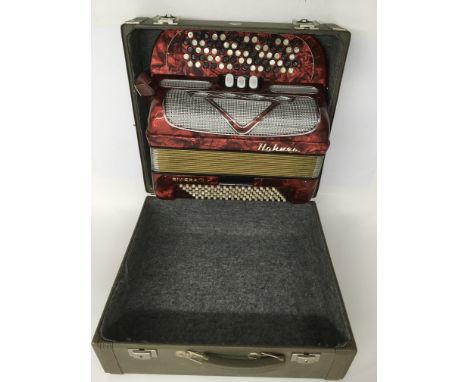 A cased Hohner Riviera II accordion in a marbled red finish.