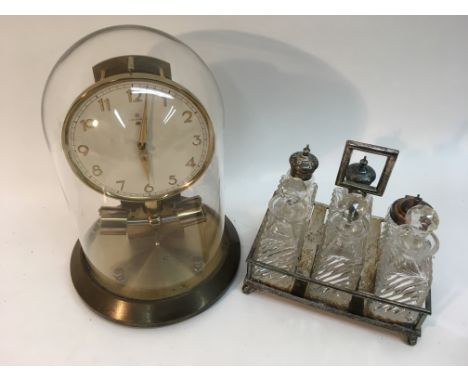 A Junghans electric clock under glass dome.Approximately 29cm high.Sold with a silver plated bottle set