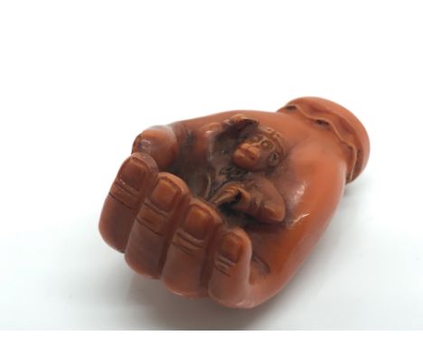A stained ivory Netsuke formed as a hand concealing a monkey.Approximately 4.5cm long