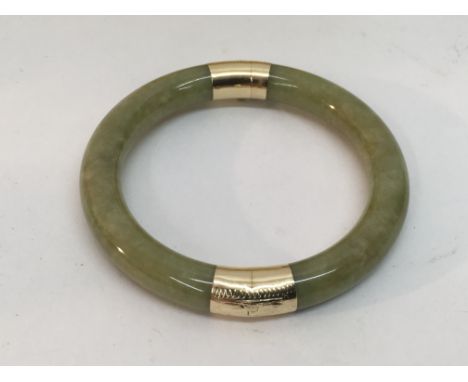 A Burmese jade bangle with 14ct yellow gold mounts.