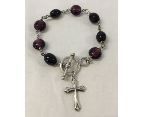 A silver bracelet with purple glass beads, a cross and T bar fastening.