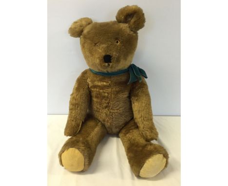 A vintage c.1920s straw filled teddy bear, approx 26 inches tall with plush fur and blue bow. Growler not working.