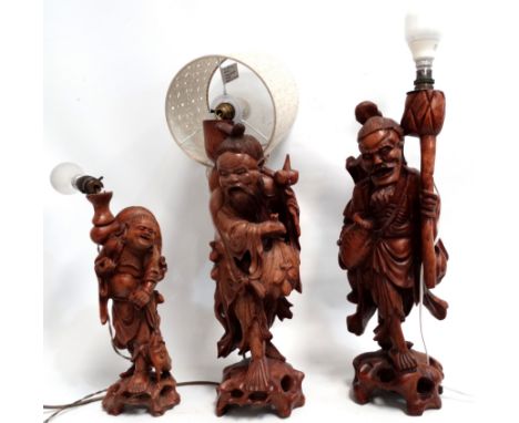 A carved hardwood lamp base - modelled in the form of a street vendor, together with another similar and a third associated, 
