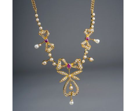 An Edwardian yellow gold ruby and seed pearl necklace, three pearl-set bow motifs each centered with a ruby and pearl drops, 