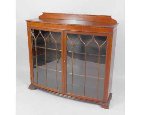 An early 20thC mahogany bow fronted bookcase, with a pair of astragal glazed doors enclosing two shelves, raised on bracket f