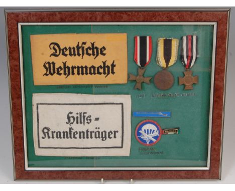 A framed and glazed display group to include, WW II German Service of the Armed Forces and Stretcher Bearers armbands, WW II 