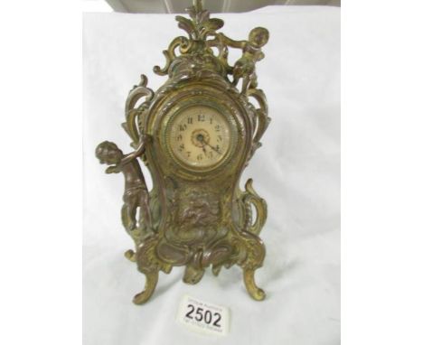 A heavy brass mantel clock surmounted cherubs.