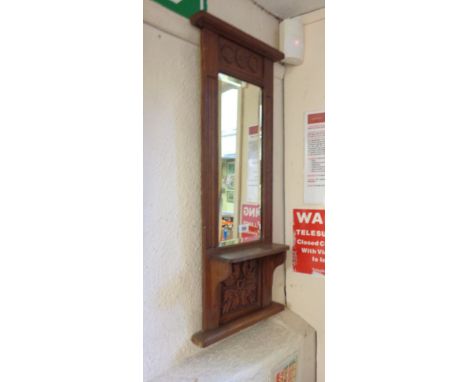 An early 20th Century carved oak framed hall mirror with decorative panel, narrow bevelled oblong plate and shelf under