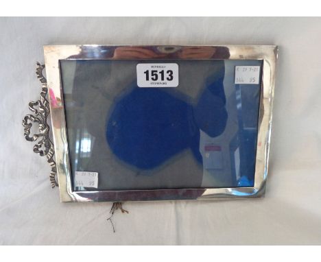 A silver fronted photograph frame with cast ribbon pattern pediment - to take 20cm X 14cm - easel stand missing