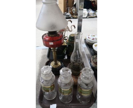 Three chemists storage jars with glass labels, a brass and cranberry oil lamp with frosted shade and a copper oil lamp Condit