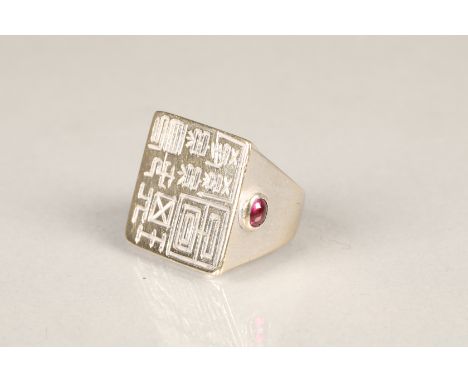 18ct white gold gents signet ring, square top etched with characters and set with a small cabochon ruby to the side. There is