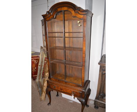 An early 20th Century Dutch style mahogany display cabinet with shaped top and shaped glazed panel door enclosing shelves wit