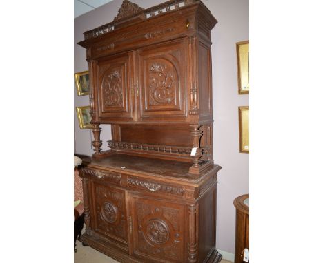A late 19th Century Flemish oak cupboard, the flared cornice with decorative carved finial above two heavily carved panel doo