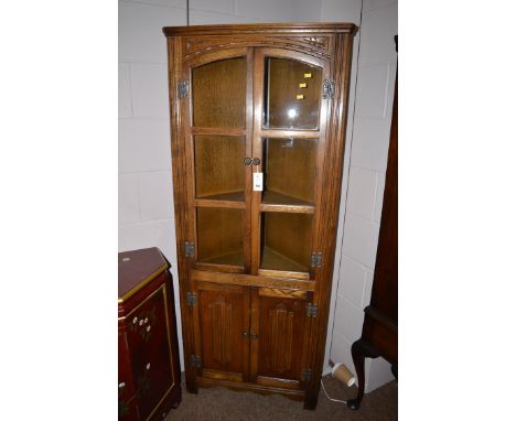 A reproduction oak standing corner cupboard, fitted two glazed doors and two linen fold panel doors below.