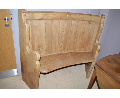 A 19th Century curved pitch pine settle with shaped ends and solid seat and panel back.