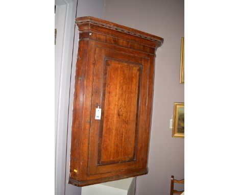 An early 19th Century inlaid oak wall hanging corner cupboard, with flared cornice over a single panel door with inlaid centr