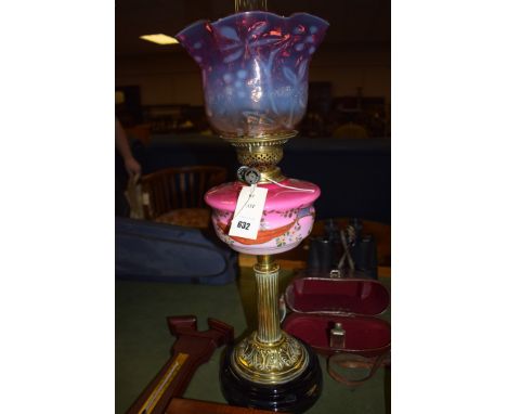 A Victorian brass oil lamp with opaque glass reservoir and cranberry glass shade.