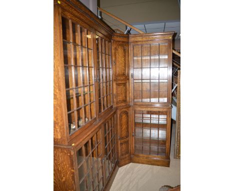 A mid 20th Century oak corner bookcase with flared dentil cornice, the left-hand side with two glazed panel doors enclosing g