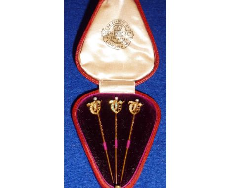 A late 19th/early 20th Century red Morocco cased set of three yellow metal Stick Pins, the finials as ancient script style in