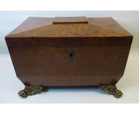 An early 19th century birds eye maple sarcophagus shape Tea Caddy with gilt metal ring handles and paw feet, the interior fit