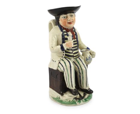 A Staffordshire pearlware sailor Toby jug, c.1800-10, seated on a sea-chest, holding a cup in his right hand and a jug in his