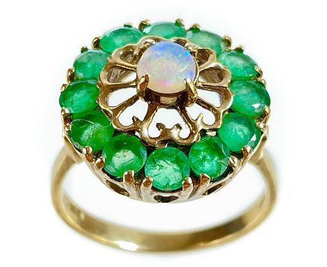 A 9ct gold emerald and opal set ring. The central blue opal measuring 4.5mm in an openwork setting, surrounded by 12 round cu