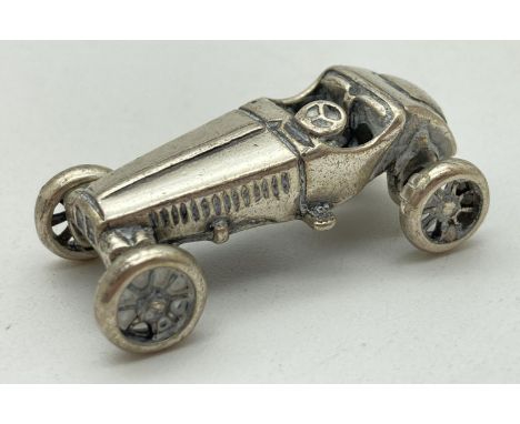 A miniature silver model of veteran racing car, with moving wheels. Stamped to underside '975 AR'. Approx. 3.5cm long and wei