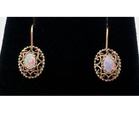 A pair of 9ct gold opal set drop style earrings. Central oval cut opal in a pierced work scroll detail mount. Gold marks to b