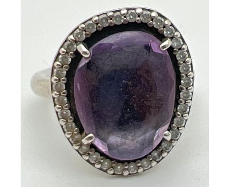 A 925 silver Glamorous Legacy ring by Pandora. Central purple faceted stone surrounded by small round cut clear stones. Insid