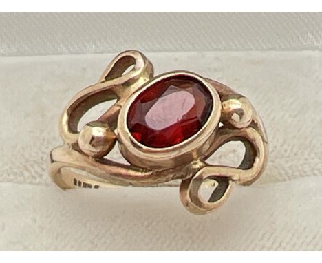 A 9ct gold and garnet contemporary design bespoke ring. Central oval cut garnet bezel set within a swirl tendril and ball des