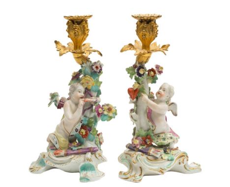 A pair of Derby gilt-metal mounted cupid candlesticks: one holding a heart, the other a bow, both with quivers below, with fl