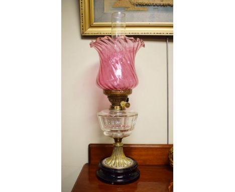 Victorian oil lamp having a facet cut clear glass reservoir, brass column and standing on a black glazed earthenware foot, ru