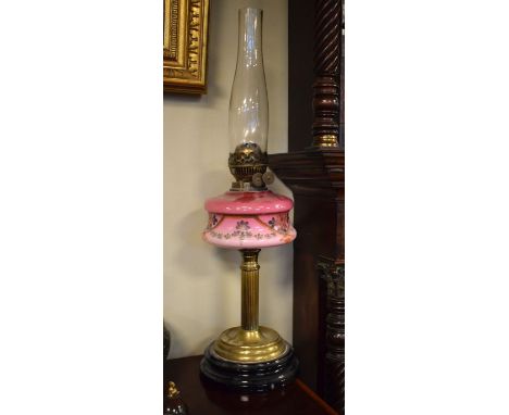 Victorian oil lamp having a pink glass reservoir with floral decoration, brass column and standing on a black glazed earthenw