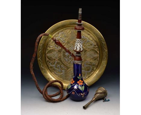 A MIDDLE EASTERN BLUE GLASS AND WOODEN HOOKAH with pipe on a brass inlaid tray, 39cm diameter