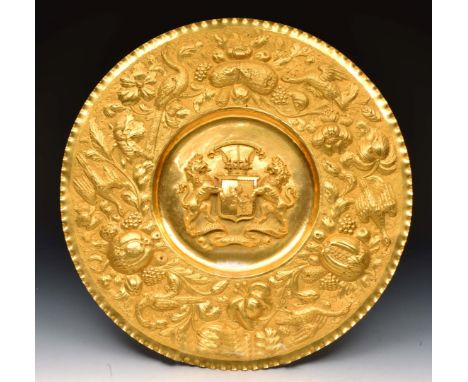 A GILDED BRASS ALMS DISH, the central coat of arms within a bird, fruit and foliate scroll broad rim, 45cm diameter