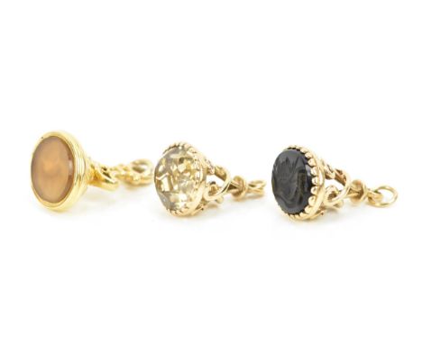 Two 9ct gold fobs and a yellow metal fob, each having pierced scroll work frames, the yellow metal fob inset with an amber co