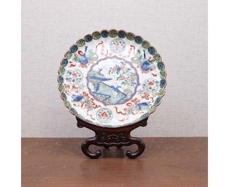 A Chinese wucai plate, Kangxi (1662-1722), of lobed form, the centre painted with a boy in a garden in a shaped panel, surrou
