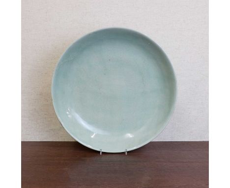 A Chinese celadon charger,the rounded sides rising from a circular foot, incised with scrolling lotus, with a six-character K