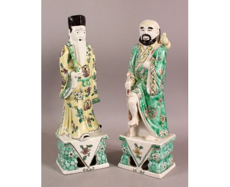 A PAIR OF CHINESE FAMILLE VERTE PORCELAIN IMMORTAL FIGURES, each figure holding a staff or stick, 32cm high.